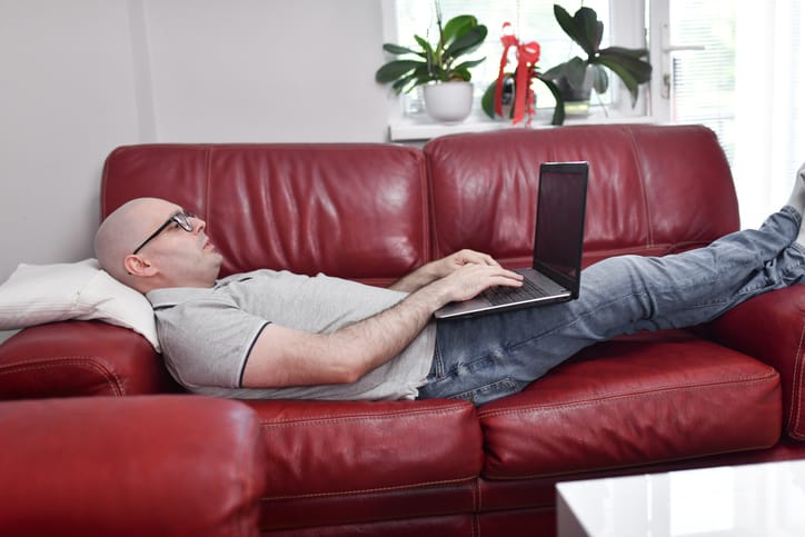 Photo shows a man with cancer lying on a sofa while researching on his computer/Getty Images
