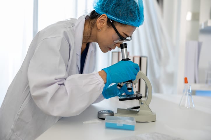 Photo shows a researcher looking into a microscope in a lab/Getty Images