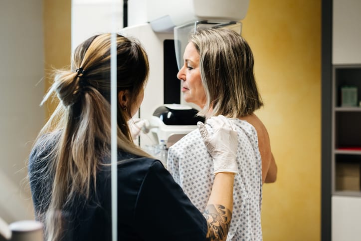 Photo shows a nurse providing assistance to a patient undergoing a mammogram in a medical facility/Getty Images