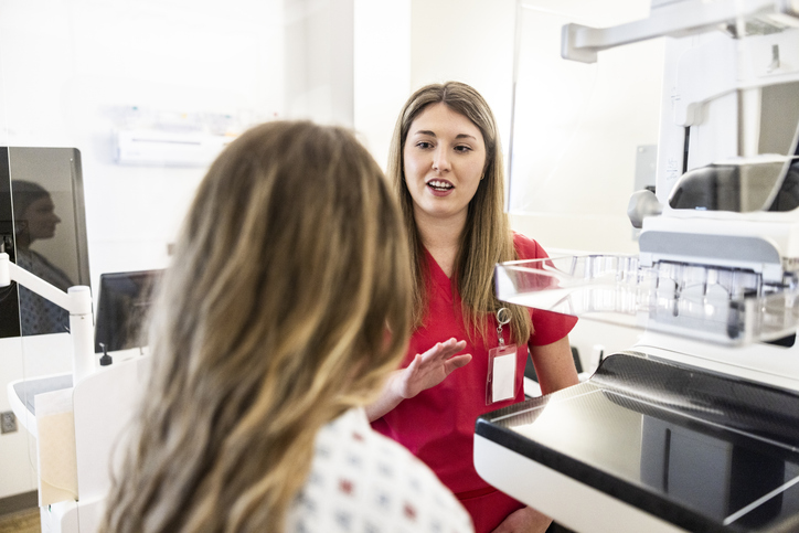 Photo shows a nurse preparing a female patient for a mammogram in a doctor's office/Getty Images