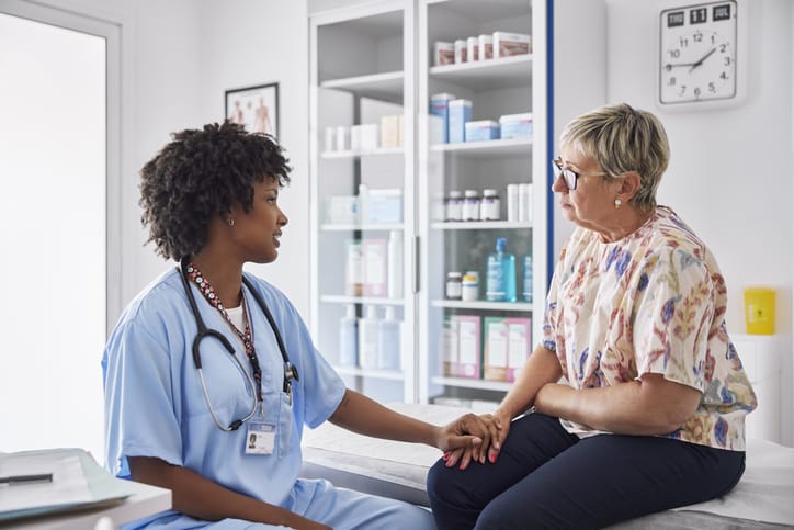 Photo shows a female healthcare worker consoling a patient sitting on examination table/Getty Images