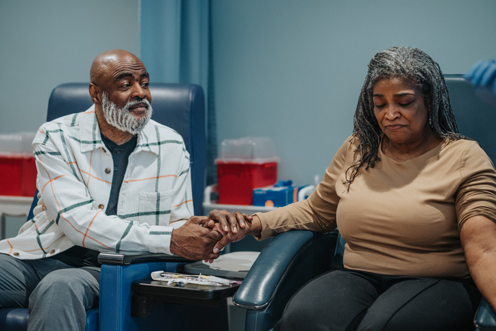 Photo shows a woman holding her husband's hand as she receives breast cancer treatment/Getty Images