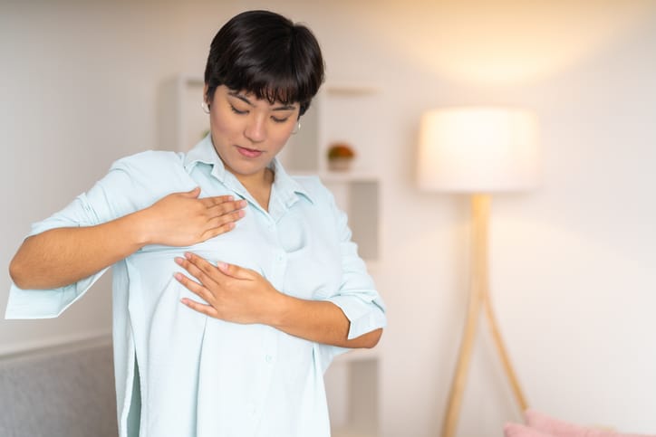 Photo shows a woman performing a self-breast exam at home/Getty Images