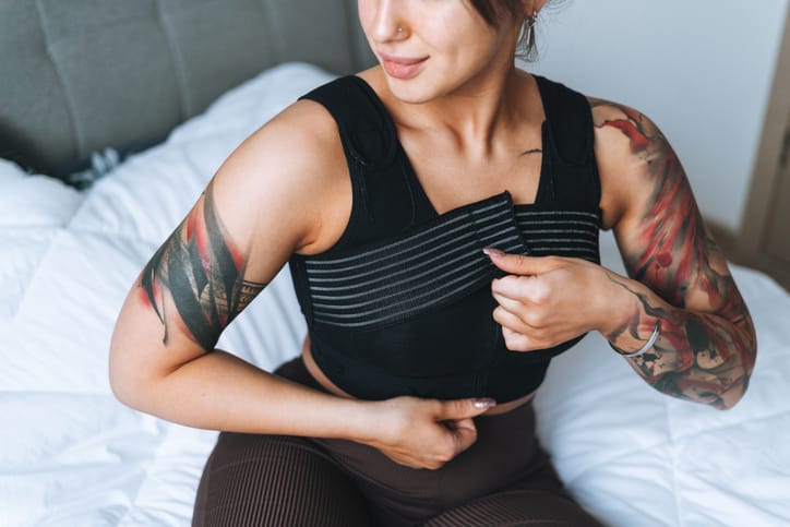 Photo shows a young woman putting a wrap on her chest after breast surgery/Getty Images