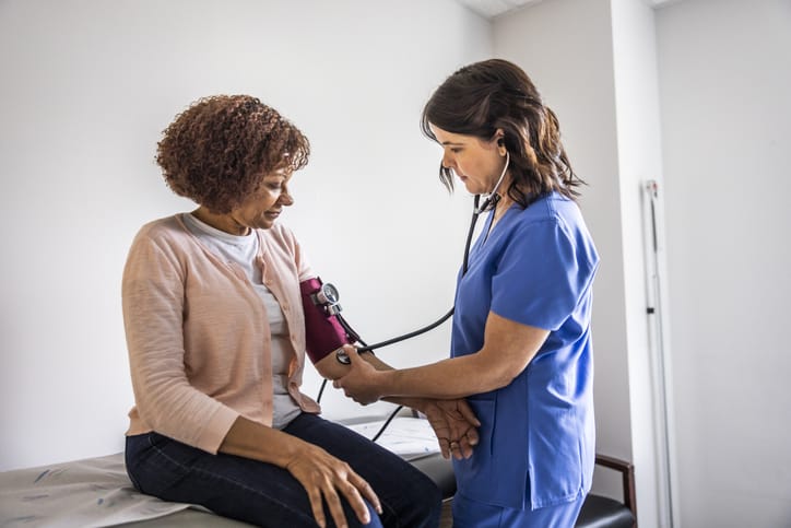 Photo shows a nurse checking a woman's blood pressure in an exam room/Getty Images
