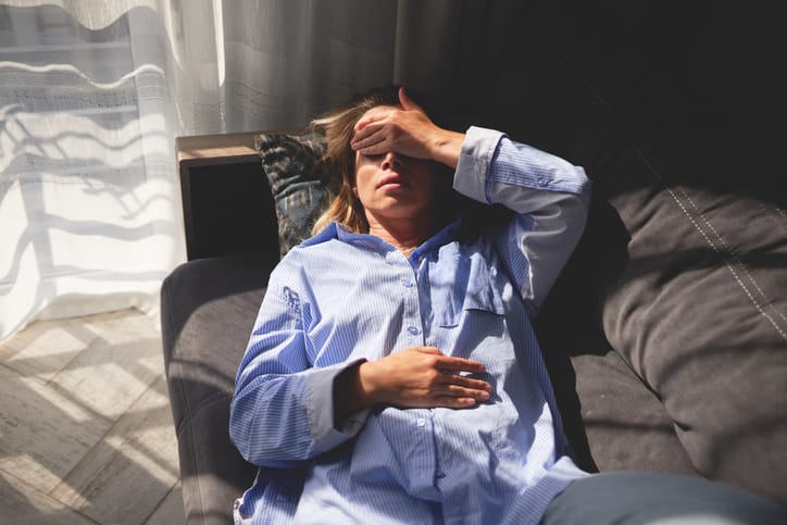 Photo shows a woman lying on a couch with her hand on her forehead and eyes closed/Getty Images