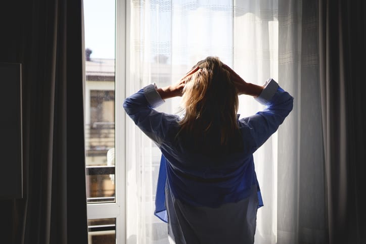 Photo shows a woman standing by a window with her hands on her head/Getty Images