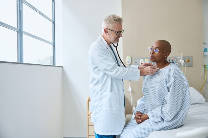 Photo shows a male doctor examining a female patient sitting on a bed at a medical facility/Getty Images