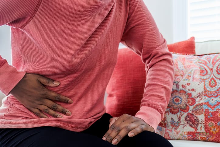 Photo shows a woman sitting on a couch and holding her stomach/Getty Images