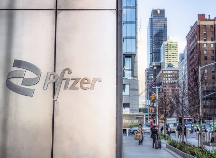 Photo shows a Pfizer sign outside their headquarters building in Midtown Manhattan, with pedestrians and traffic on the street beyond/Getty Images